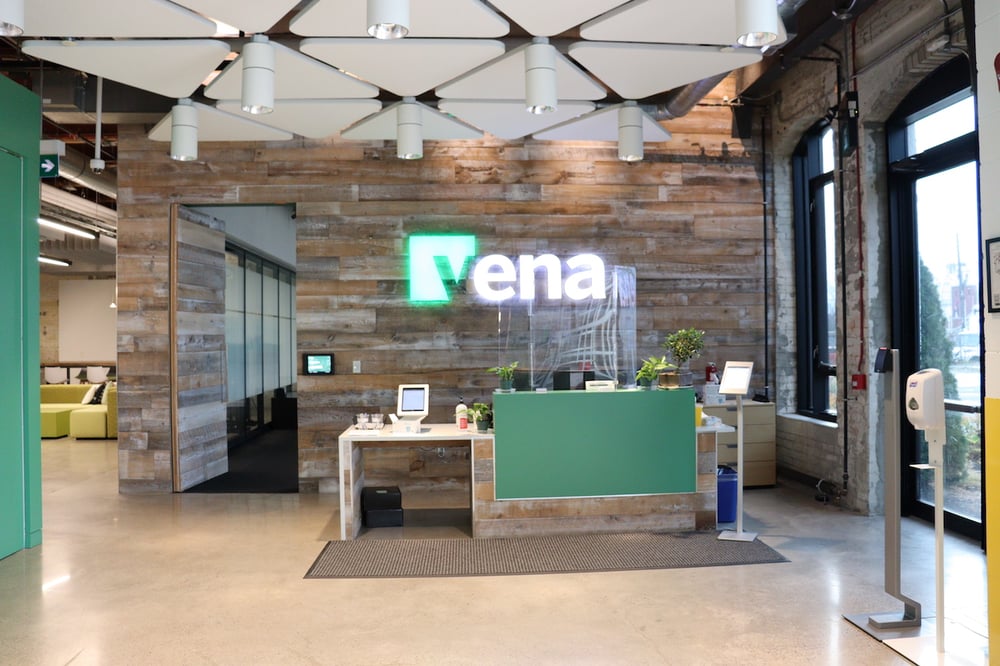 Modern office reception with plants, green accent wall, and a bright neon sign reading 